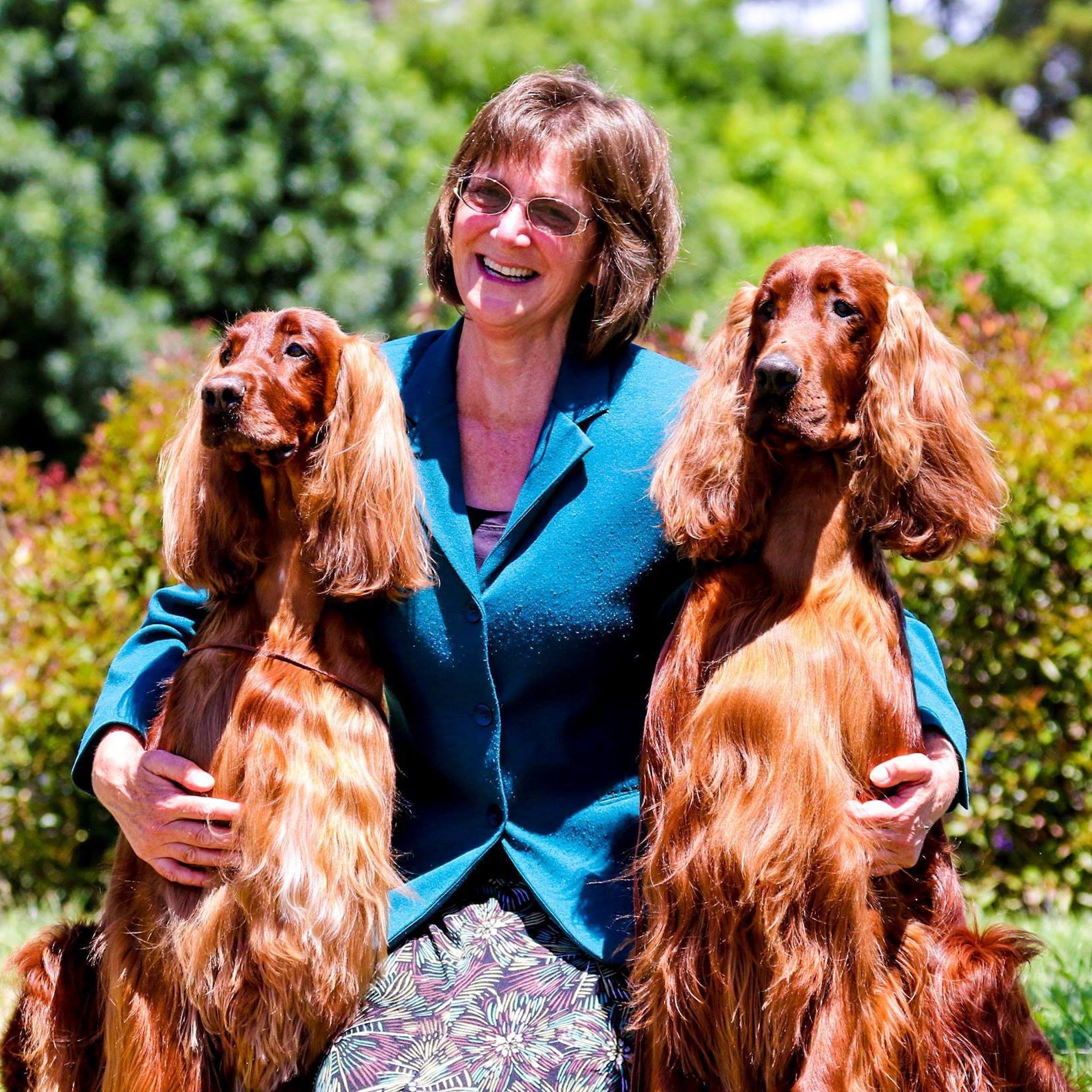 Carrie Paine kneels hugging two Irish Setter dogs at either side.